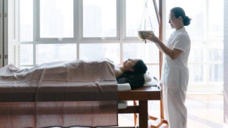 une femme allongée reçoit un massage ayurvédique à l'huile chaude sur la tête