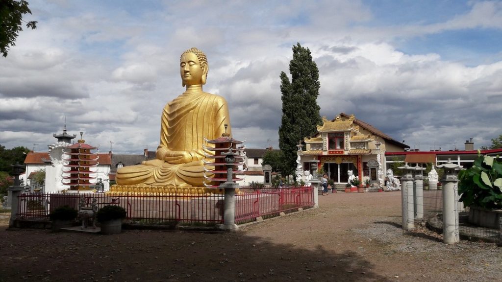 Statue doree de Bouddha haute de 7 metres dans un parc paysager d'inspiration asiatique avec la pagode de Phap-Vuong-Tu en arrière plan.
