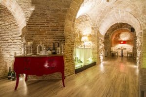 Cave à vins-restaurant à Madrid. Niches en pierre avec tables. Meuble rouge portant bouteilles, chandeliers et cloche.