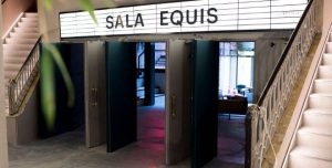 Entrée du cinéma avec inscription en grand de La Sala Equis à Madrid. Deux grandes portes doubles sont ouvertes et donnent sur l'entrée du cinéma.