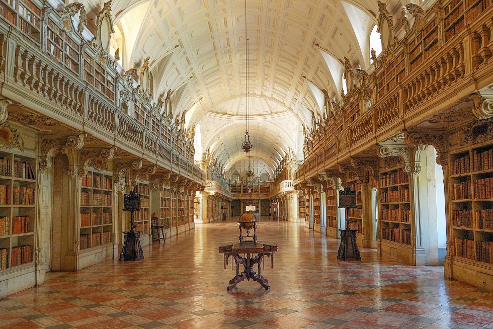 Bibliothèque de Mafra : une large et longue allée dont le sol est en marbre, avec des étagères remplies de livre de chaque côté sur 2 niveaux.