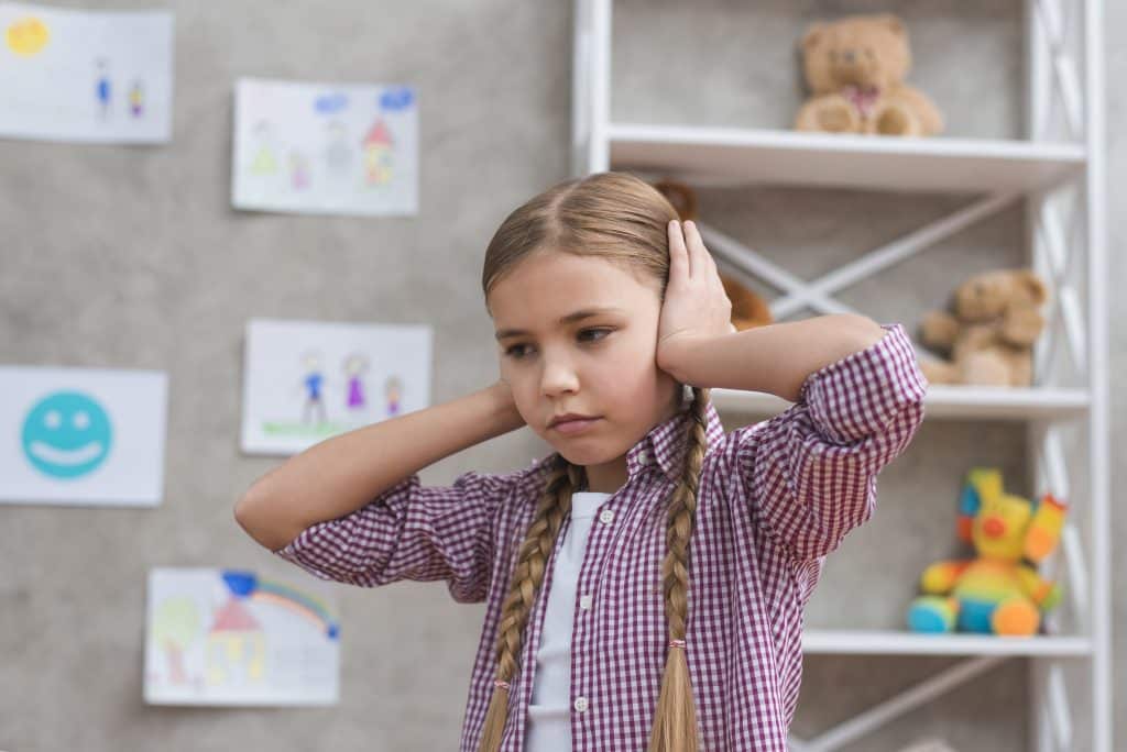 Petite fille autiste qui se bouche les oreilles à cause de son hyper-sensibilité sensorielle