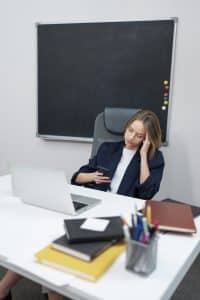 Une jeune femme dans un bureau consulte son téléphone portable plutôt que de se concentrer sur son ordinateur, face à elle.