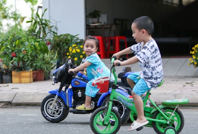 Deux petits enfants faisant le course dans la rue, la petite à moto et le petit à vélo.