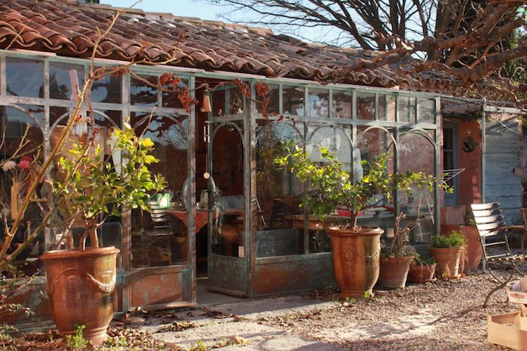 Veranda salon photographiee depuis exterieur compose de plantes dans jarres provençales dans jardin ensoleille maison entre amis