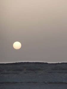 Le soleil se lève sur un désert rocailleux dans un clair-obscur gris.