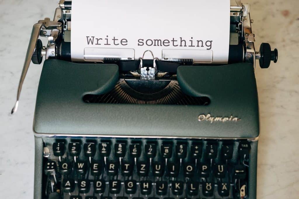 Une feuille de papier où il est inscrit " write something " est insérée dans une machine à écrire