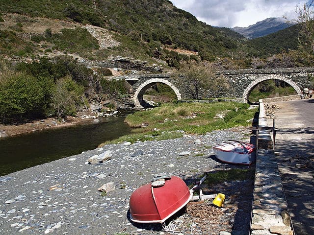 Pont génois de Negru : ancien pont de pierre à double arche surplombant un ruisseau et des barques retournées.