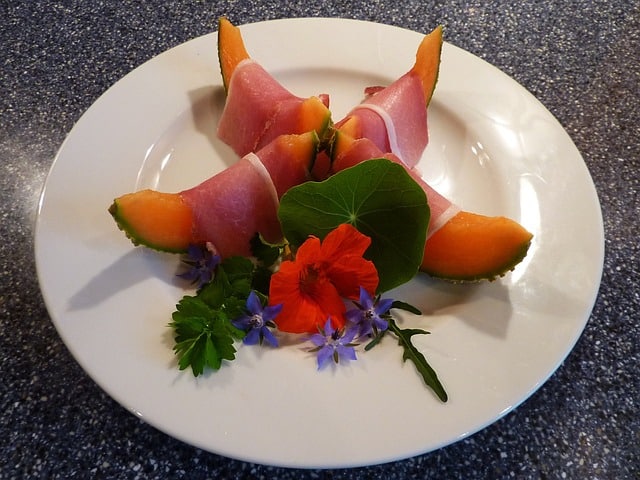 Assiette de melon au jambon décorée avec des fleurs comestibles de capucine. 